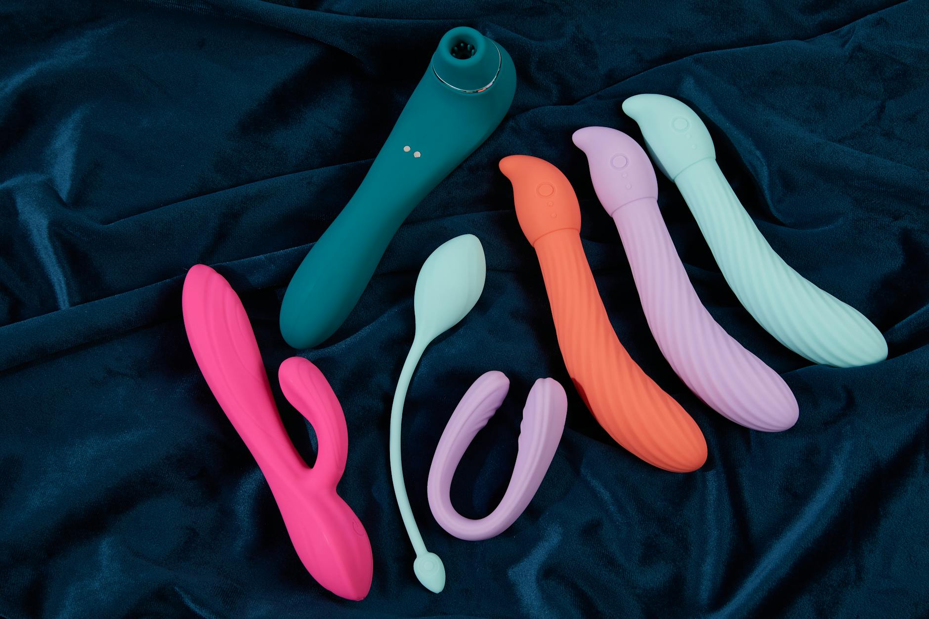 Collection of colorful silicone clitoral vibrators and external sex toys arranged on dark fabric