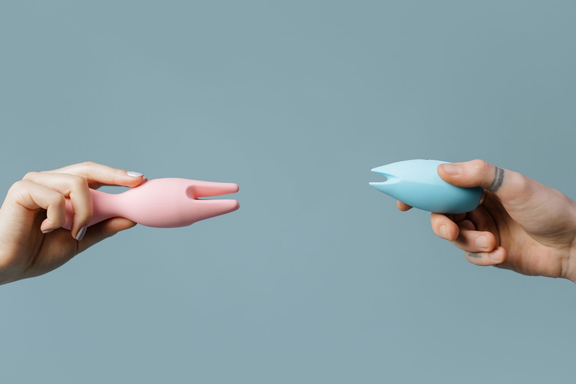 Two hands holding vibrators against a pastel background, representing options for pleasure.