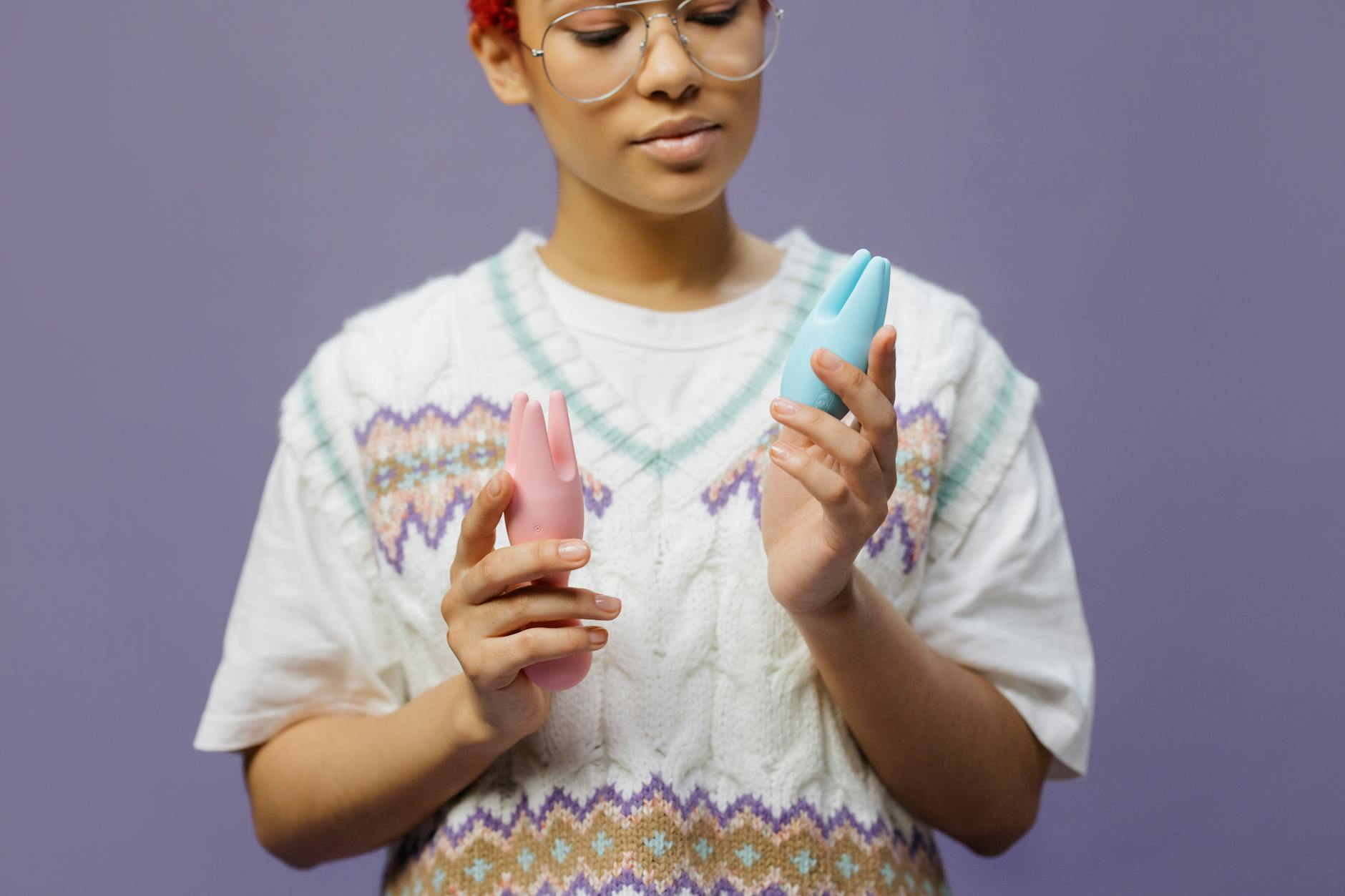Hands holding a blue personal massager against a knitted sweater, representing gentle pleasure exploration