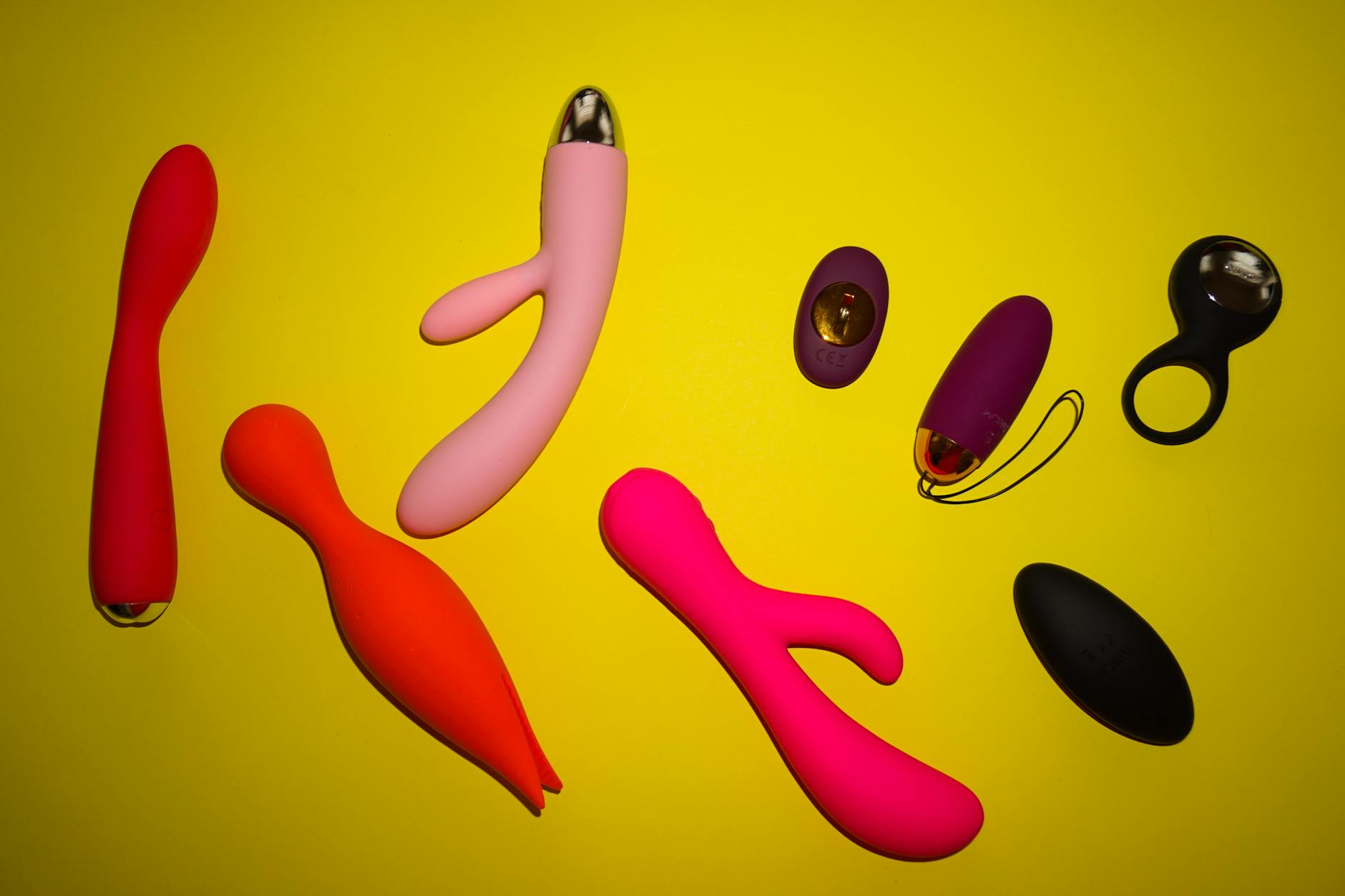 Array of vibrant adult toys displayed on a bright yellow surface, showcasing diversity and design.
