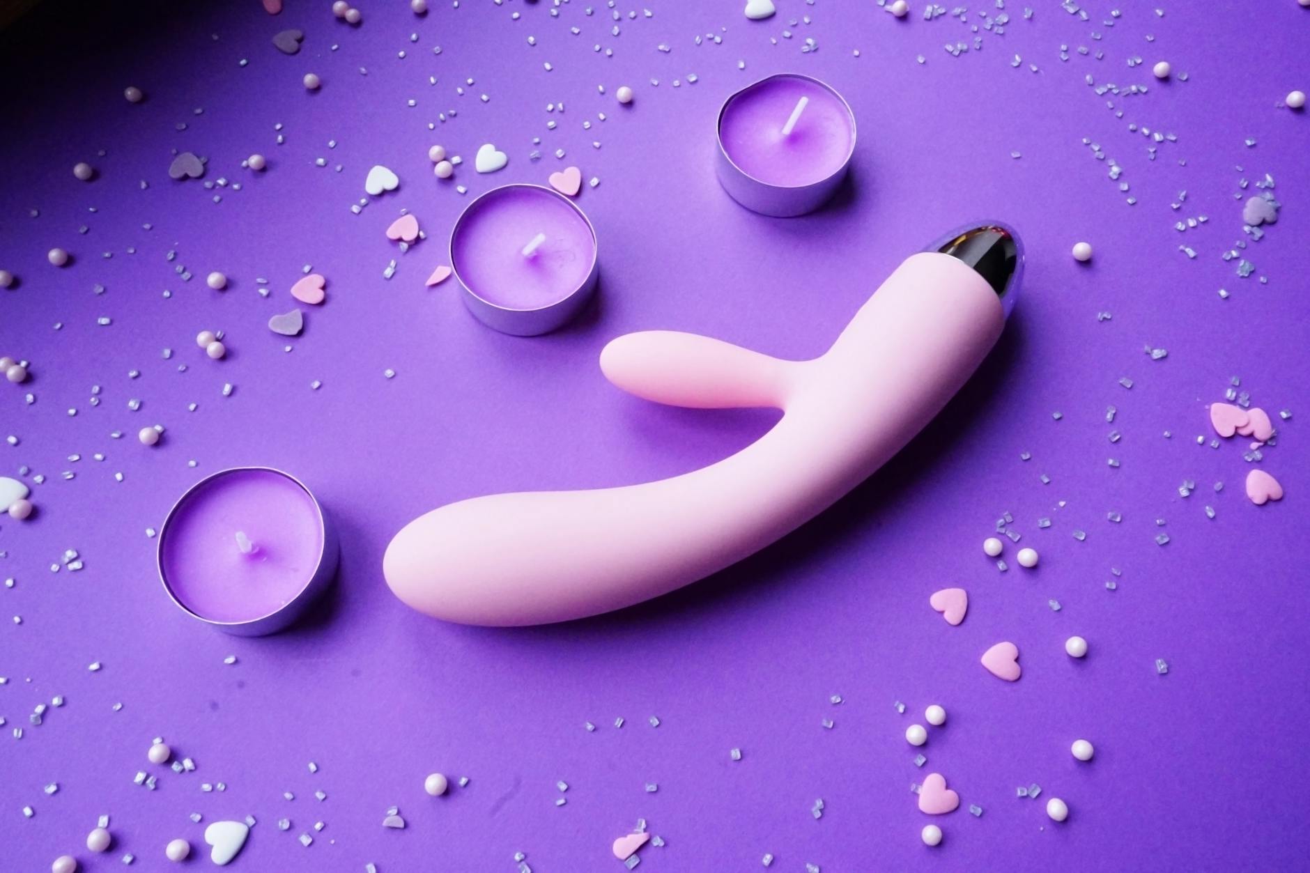 A teal clitoral vibrator displayed on soft white silk fabric