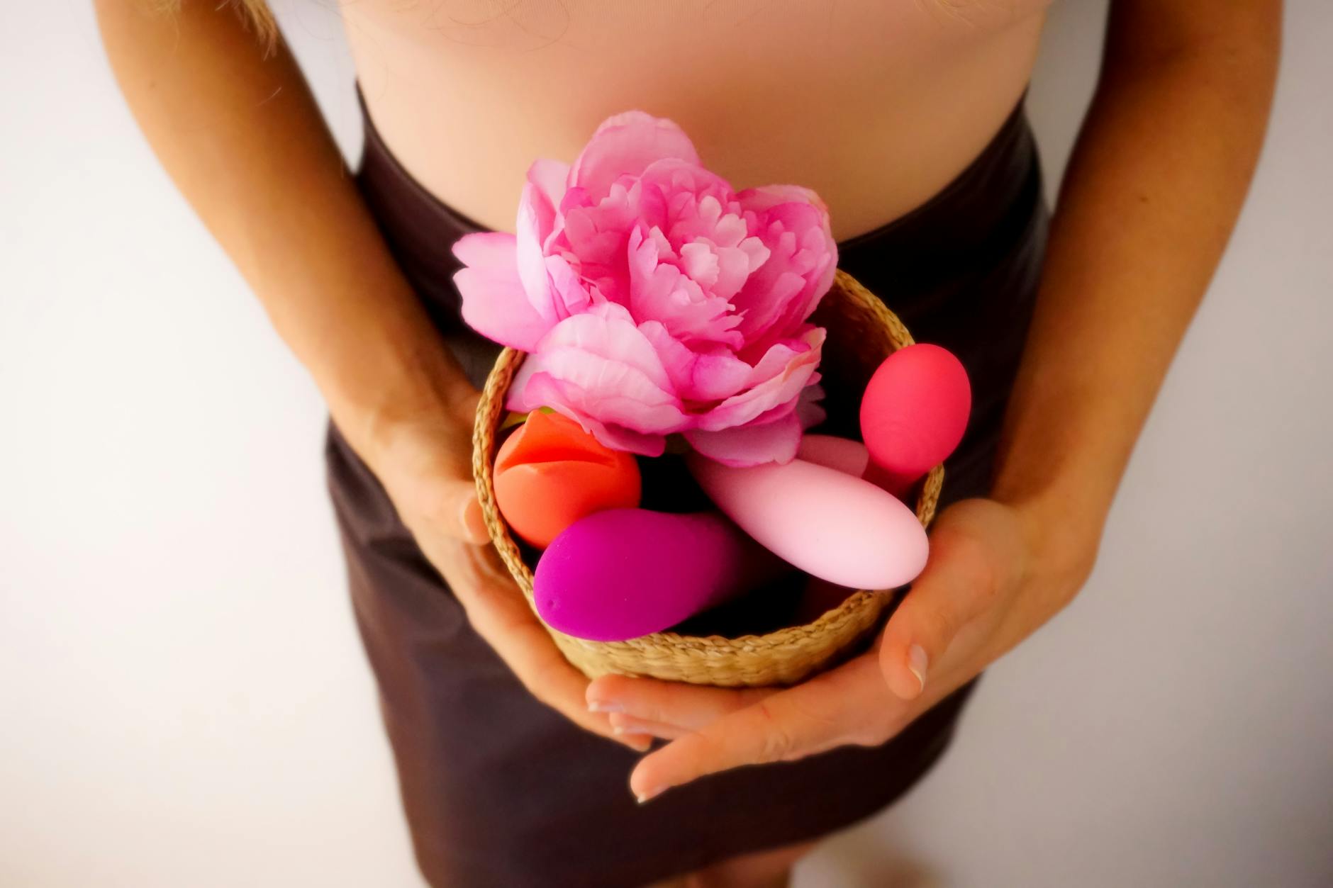 A person holding a basket containing colorful vibrators and a pink flower.